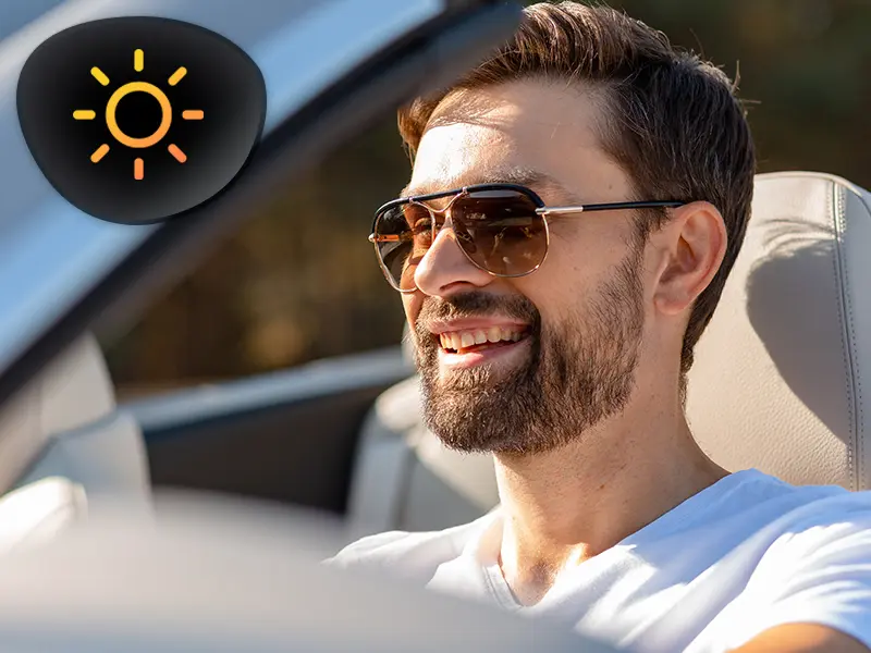 The image depicts a person driving while wearing polarized sunglasses; the lenses effectively reduce visual blurring caused by sunlight.